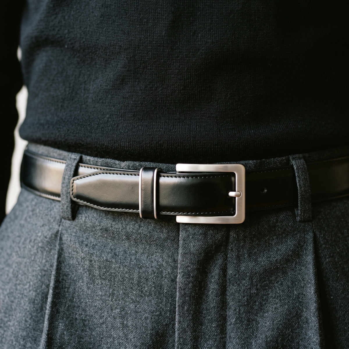 Cinturón Capital Negro puesto con suéter negro y pantalón gris de pinzas